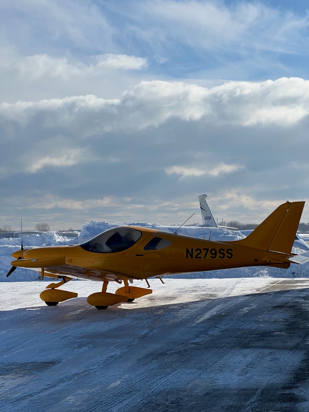 The yellow Bristell N279SS on a snow covered ramp under a broken sky