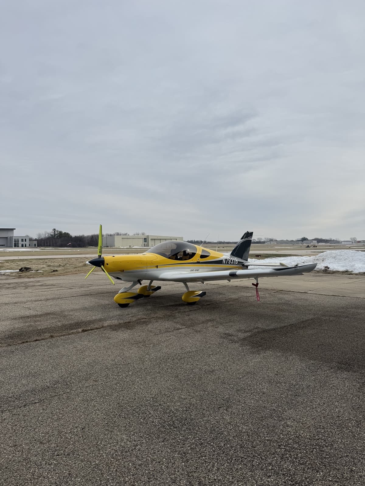 The yellow Bristell N7931B on the ramp, its black tail against a winter sky