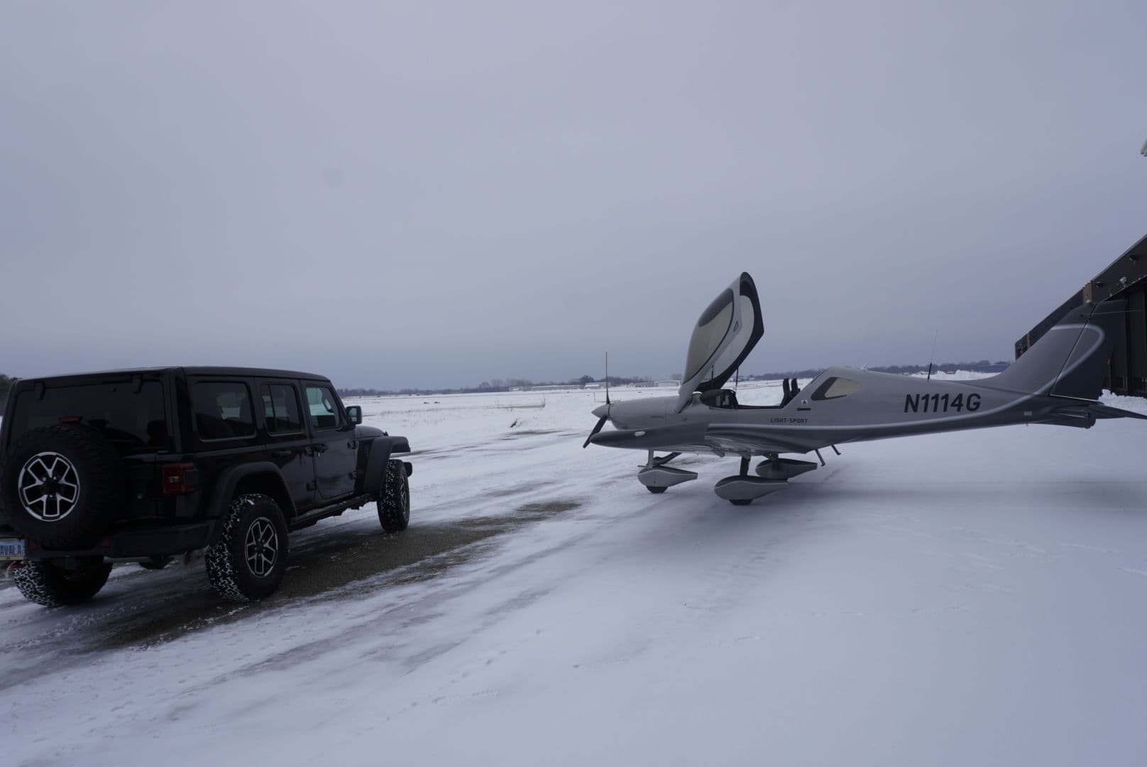 A silver Bristell on the ramp with a Jeep alongside