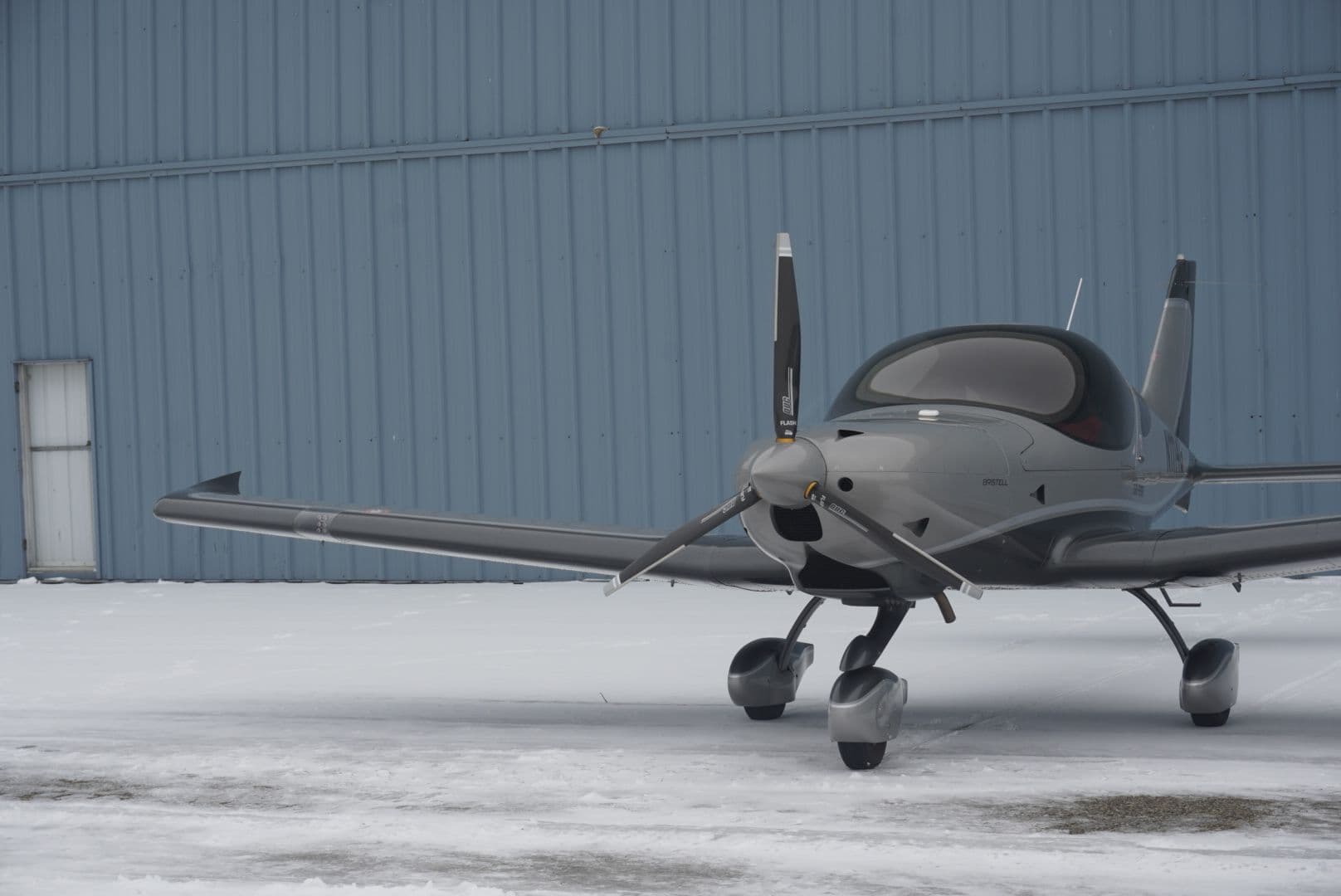 Front quarter view of a silver Bristell beside the hangar