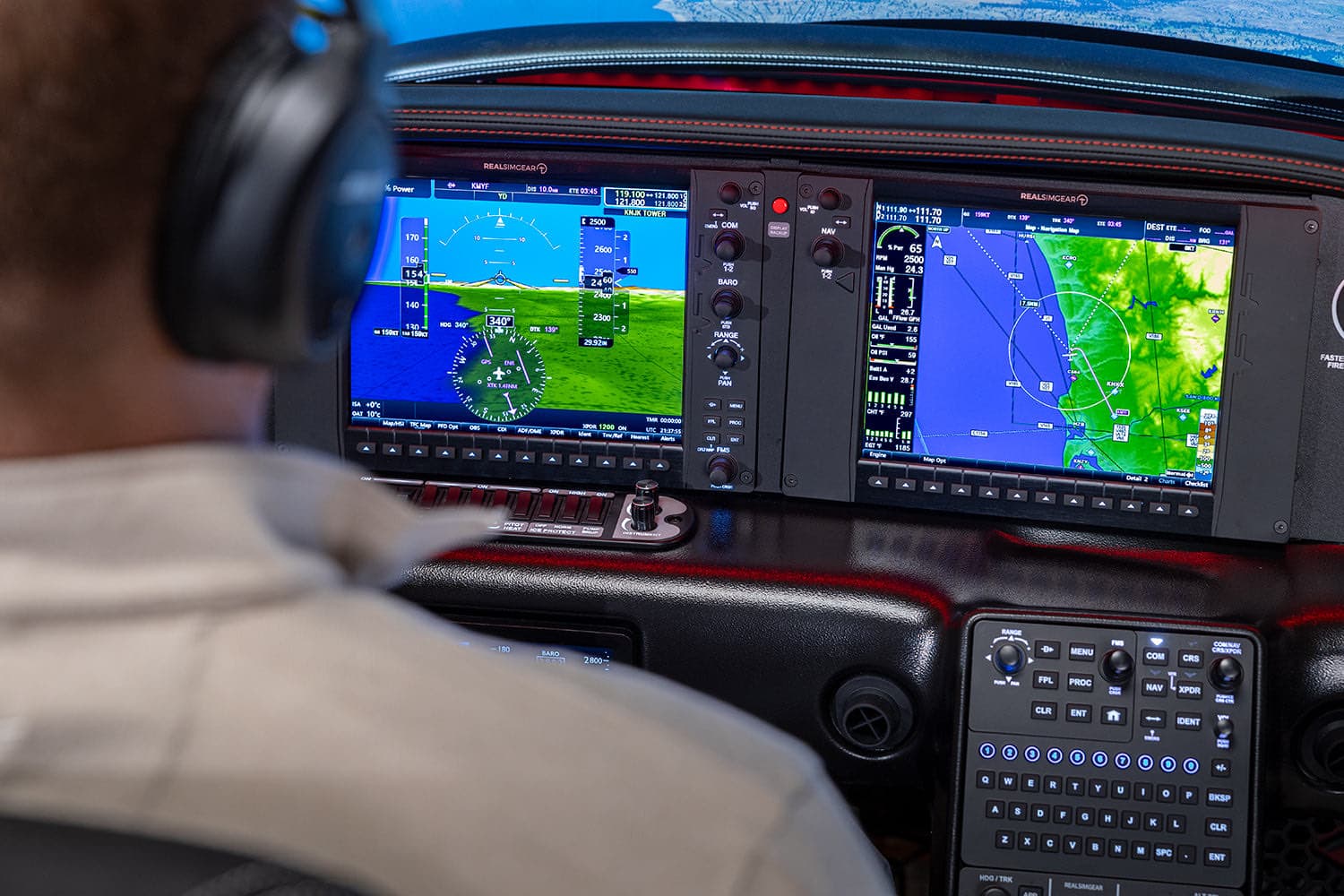 A pilot in a headset flying the RealSimGear SRx simulator, the Garmin Perspective displays lit ahead